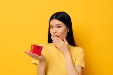 Elinde hediye kutusu olan bir kadın sarı arka plan pozu veriyor.