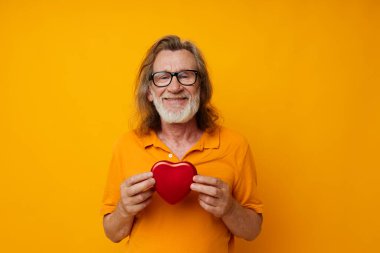 Emekli yaşlı adamın fotoğrafı sarı tişört ve gözlükler kalp şeklinde kutu sarısı arka plan pozu veriyor.