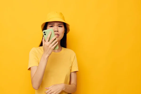 노란 모자를 쓰고 티셔츠를 입은 여성 이 아무런 변화 없이 전화로 노란 배경에 대해 이야기하는 모습 — 스톡 사진
