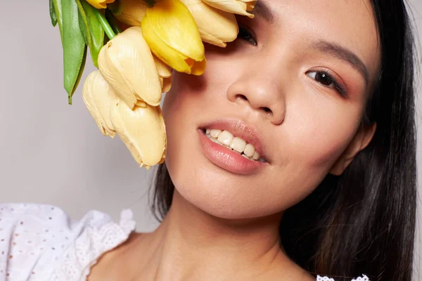 Asyalı güzel bir kadının portresi. Çiçekler. Arka planda hafif bir poz veriyor. — Stok fotoğraf
