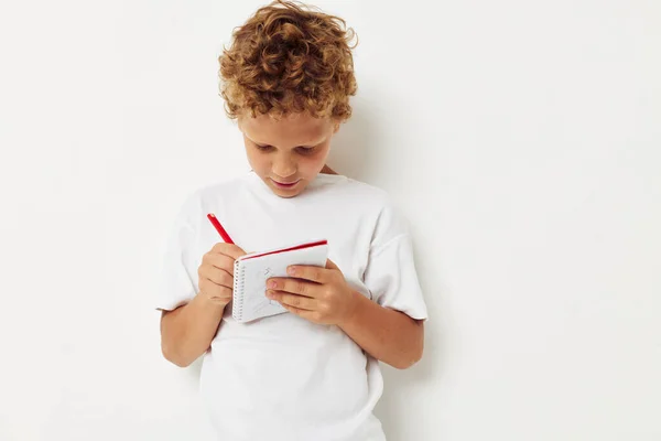 Um menino alegre com cabelo encaracolado desenha em um caderno com um lápis Imagem De Stock