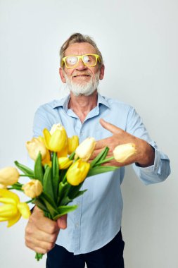 Emekli yaşlı bir adamın fotoğrafı. Bir buket çiçek. Hediye olarak hafif bir arka plan.