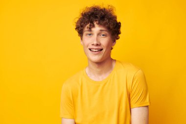 Şık sarı tişört giyen genç bir kıvırcık adamın portresi tek renkli poz veriyor.