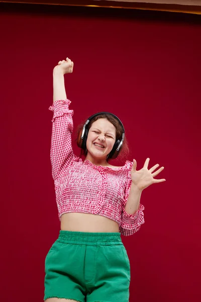 Pretty woman in pink blouse and green shorts with headphones listening to music — Fotografia de Stock