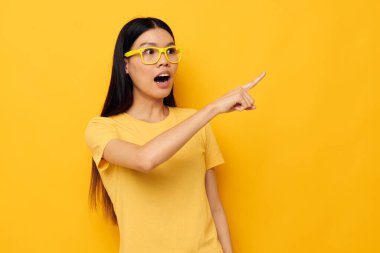 Büyüleyici genç Asyalı gözlüklü kadın, el kol hareketi yapıyor. Fotokopi alanı sarı arka planı değişmemiş.