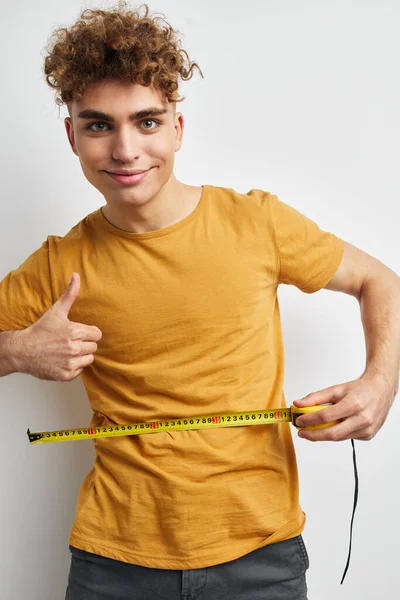 Aantrekkelijke man meten tape meten in geel t-shirt lichte achtergrond — Stockfoto