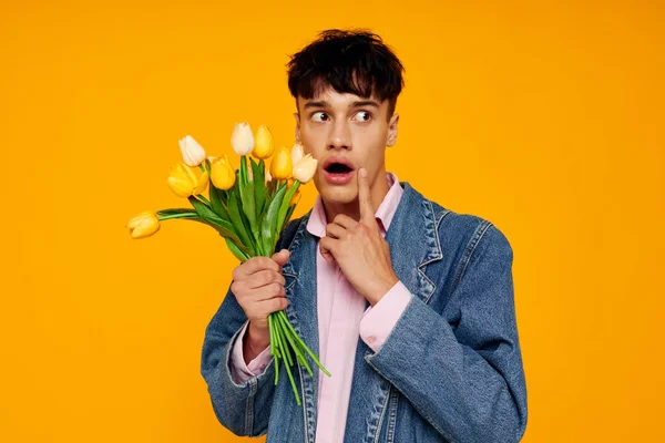 Hombre guapo con ramo de flores en chaqueta denim moda fondo amarillo — Foto de Stock
