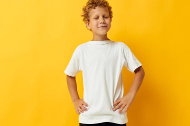 Sarı arka planda beyaz tişörtlü kıvırcık saçlı çocuk.