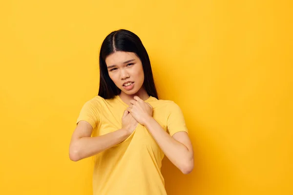 Charming young Asian woman in a yellow t-shirt holding his head discontent yellow background unaltered — Stockfoto