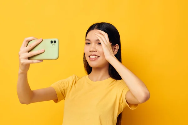 노란 티셔츠를 입은 젊은 아시아 여성 이 변경되지 않은 생활 방식을 보여 주는 전화를 보고 있는 모습 — 스톡 사진
