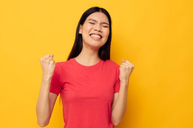 Kırmızı tişörtlü Asyalı güzel bir kadının portresi. Duygular poz veriyor. Sarı arka plan değiştirilmemiş.