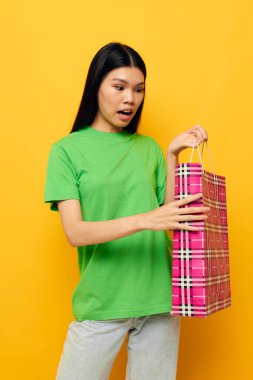 Çekici Asyalı genç kadın alışveriş paketi sarı arka plan değiştirilmemiş