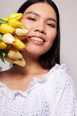 Asyalı güzel bir kadının portresi. Çiçekler. Arka planda hafif bir poz veriyor.