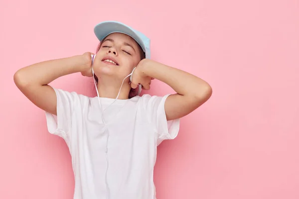 Aranyos lány fejhallgató egy fehér póló és sapka rózsaszín háttér — Stock Fotó