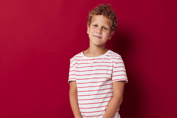 Веселый мальчик в полосатой футболке жесты с руками красный фон