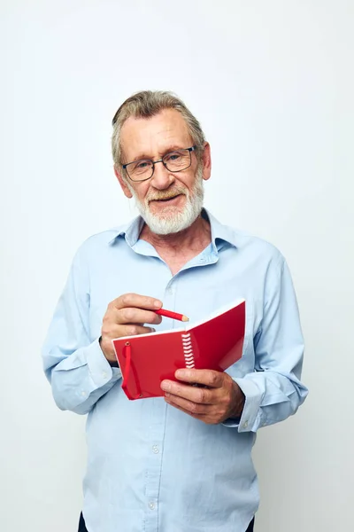 Ritratto di uomo anziano felice con notebook rosso e penna sfondo chiaro — Foto Stock