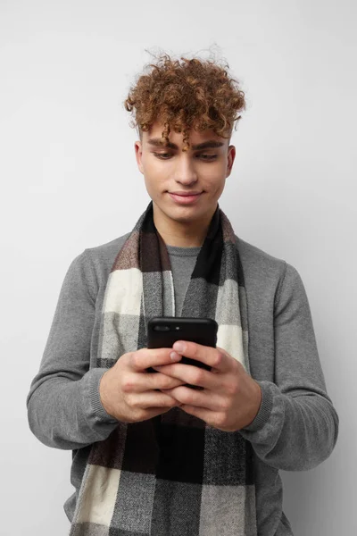 Красивий молодий чоловік в шарфі, дивлячись на модний світлий фон телефону — стокове фото