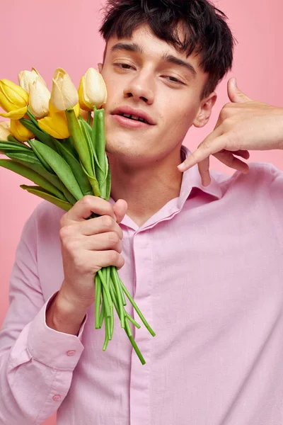 Chico guapo en una camisa rosa con un ramo de flores haciendo gestos con las manos aisladas fondo inalterado —  Fotos de Stock