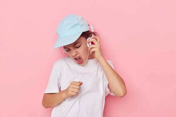 흰색 티셔츠를 입고 분홍색 모자를 쓰고 있는 어린 소녀 헤드폰 — 스톡 사진