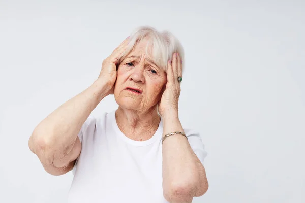 Emotional elderly woman in a white t-shirt headache health problems light background — Stock Photo, Image