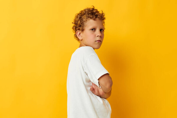 Весёлый мальчик в белой футболке позирует студийному жёлтому фоне