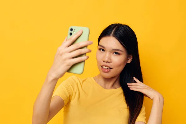 Donna con un telefono tra le mani fa un selfie sfondo giallo inalterato — Foto Stock