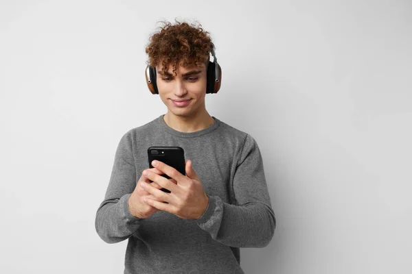 Kinky guy with a phone in hand listening to music in headphones light background — Stock Photo, Image