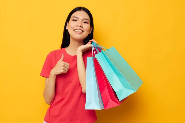 Vrouw met aziatische uitstraling shopping tassen in rood t-shirt geïsoleerde achtergrond ongewijzigd — Stockfoto