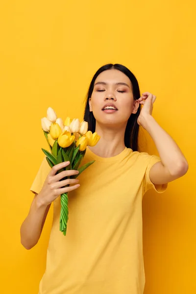 Vacker brunett bukett med blommor i händerna våren kul poserar gul bakgrund oförändrad — Stockfoto