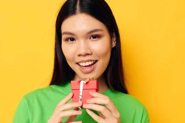 Woman with Asian appearance in green T-shirts with a small gift box yellow background unaltered — 图库照片