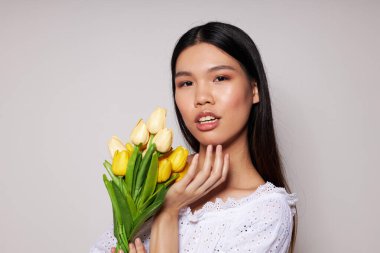 Bir buket çiçekle Asyalı bir kadın yakın çekim stüdyo modelini değiştirmeden gülümsüyor.