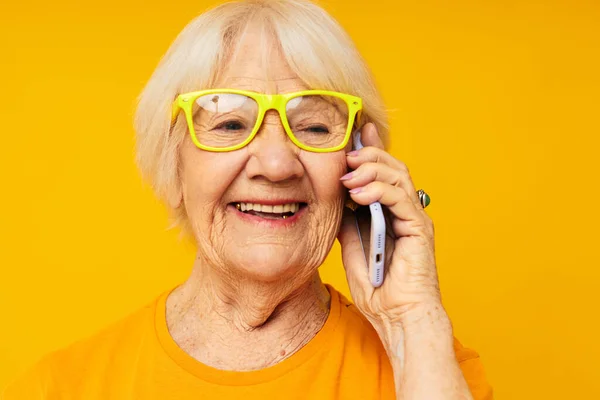 Улыбающаяся пожилая женщина разговаривает по телефону в желтых очках изолированный фон — стоковое фото