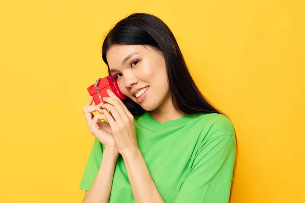 Woman with Asian appearance in green T-shirts with a small gift box yellow background unaltered — 图库照片