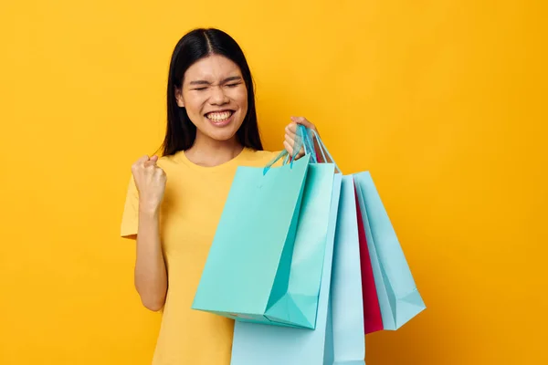 Portret Aziatische mooie jonge vrouw in een geel T-shirt met veelkleurige boodschappentassen studio model ongewijzigd — Stockfoto