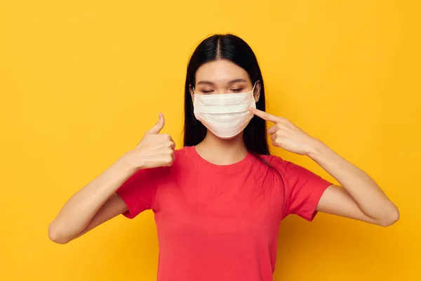 Encantador jovem mulher asiática em vermelho t-shirt máscara médica proteção amarelo fundo inalterado — Fotografia de Stock