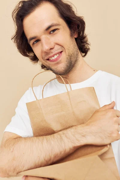 Man in a white T-shirt with paper bag beige background — Stockfoto