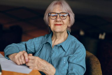 Mutlu kıdemli kadın çalışma kâğıdı ve kalem kağıtlarını değiştirilmemiş yaşam tarzıyla belgeliyor.