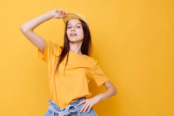 Optimistisk ung kvinna poserar i en gul T-shirt och mössa gul bakgrund — Stockfoto