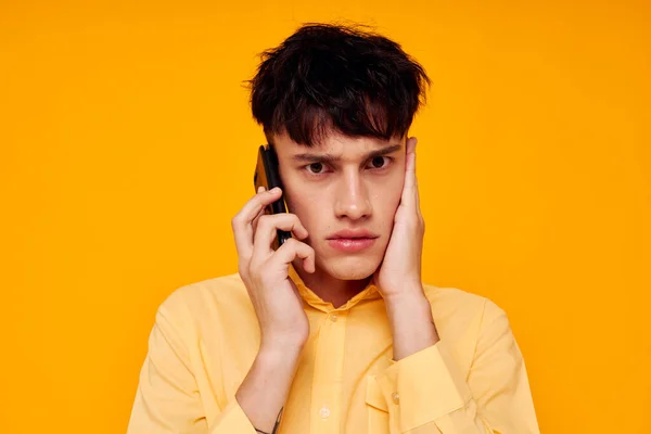 Молодий хлопець в жовтій сорочці говорить по телефону ізольований фон — стокове фото