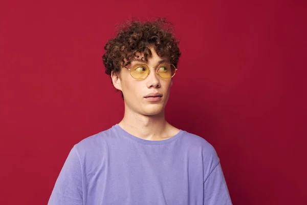 Молодий кучерявий чоловік в жовтих окулярах фіолетові футболки емоції червоний фон — стокове фото