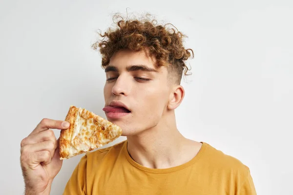 Handsome guy in a yellow t-shirt eating pizza isolated background — 图库照片