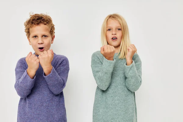 Niño y niña en suéteres multicolores posando para un fondo claro divertido — Foto de Stock