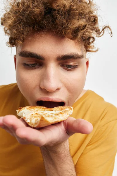 Schöner junger Mann, der Pizza isst und dabei in Nahaufnahme posiert — Stockfoto