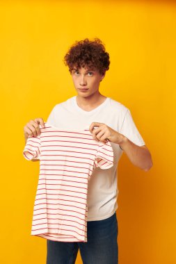 Beyaz tişörtlü, kırmızı kıvırcık saçlı adam çizgili tişört giyiyor. Gençlik tarzı, sarı arka plan değiştirilmemiş.
