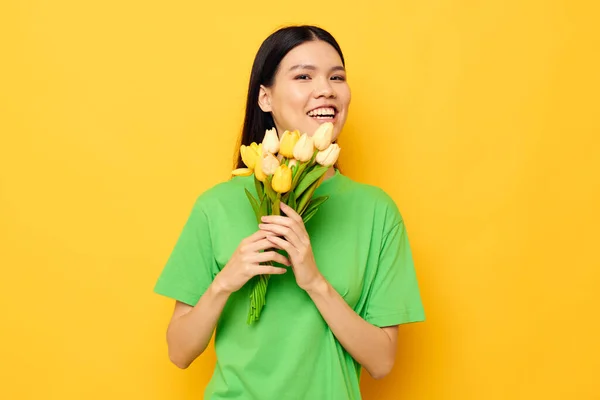 젊은 아시아 여성 녹색 티셔츠를 입고 아무런 변화가 없는 배경 배경에 노란 꽃들 이 만 발 한 꽃다발 — 스톡 사진