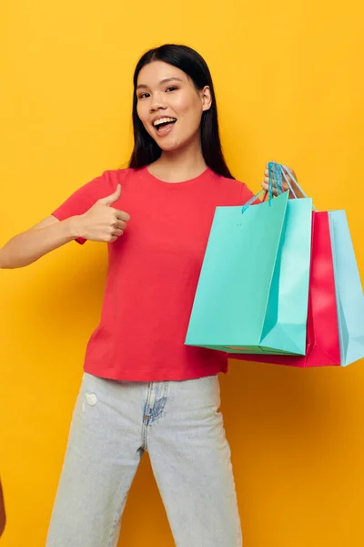 Urocza młoda Azjatka z kolorowymi torbami pozowanie zakupy zabawy żółty tło bez zmian — Zdjęcie stockowe