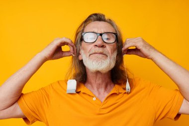 Çay poşetleri olan yaşlı bir adam sarı arka planda poz veriyor.