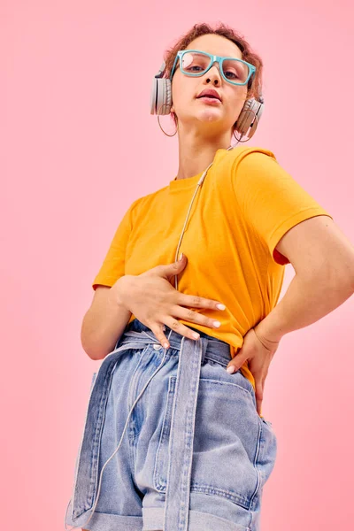 Красивая женщина желтые наушники футболки развлекательная музыка весело розовый фон без изменений — стоковое фото