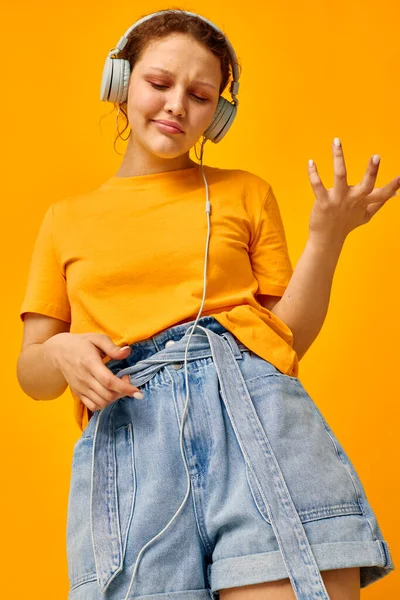 Pretty woman yellow t-shirt headphones entertainment music fun yellow background unaltered — Stockfoto