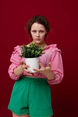 Pembe bluzlu çekici bir kadın beyaz tenceredeki bir bitkiyle poz veriyor.